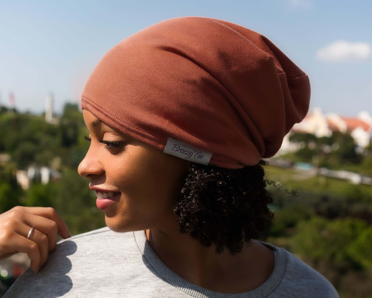 woman wearing a Satin-Lined Beanie for Women and Men - Soft and Warm Beanie with Satin Lining to Protect Hair in Burnt Orange.  She is shown in profile against a blurred outdoor background of green hills and blue sky.