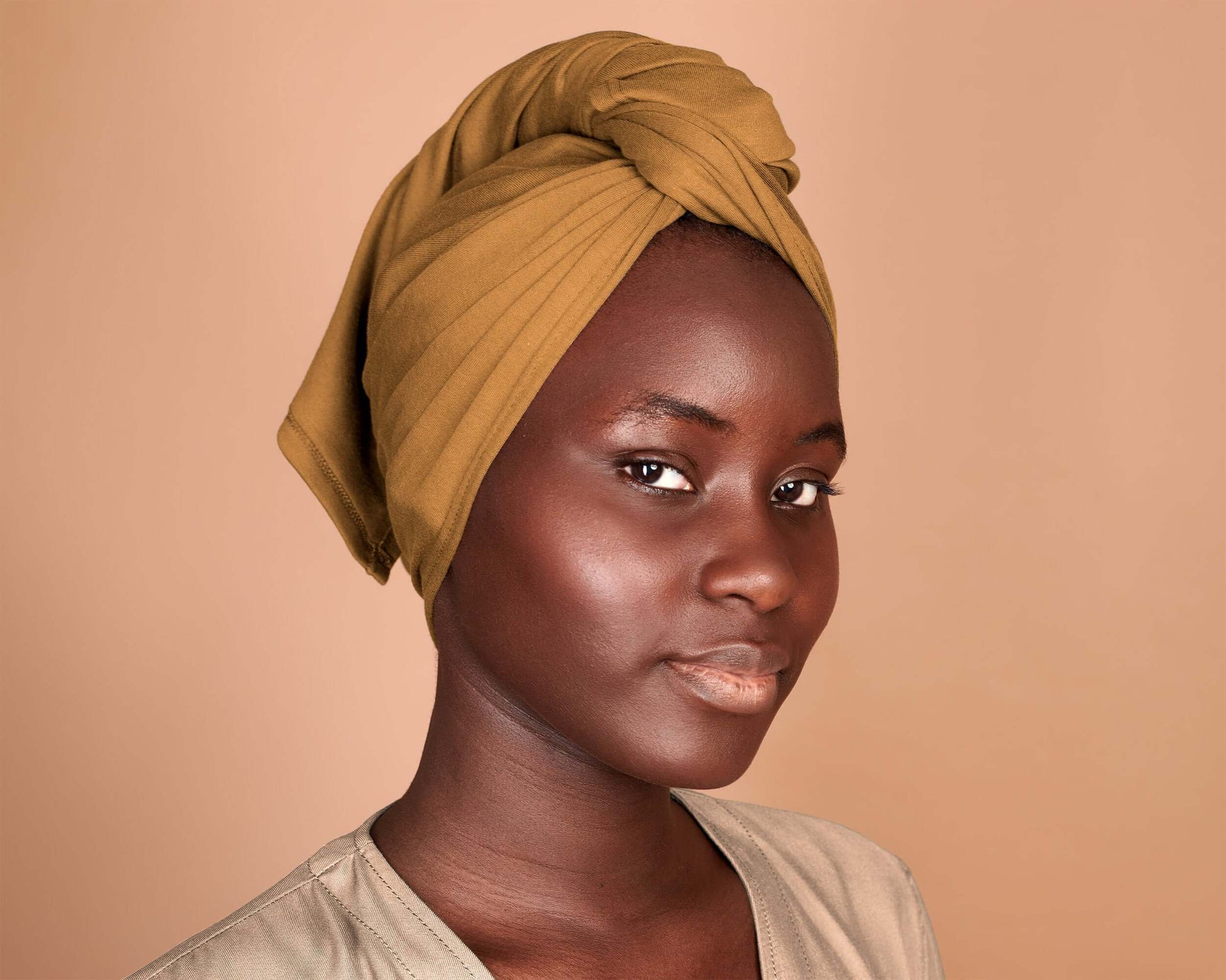 Woman with curly hair plopping a T-Shirt Hair Towel for Curly, Wavy, and Straight Hair - Soft, Absorbent, and Eco-Friendly in mustard yellow,  in a beige background