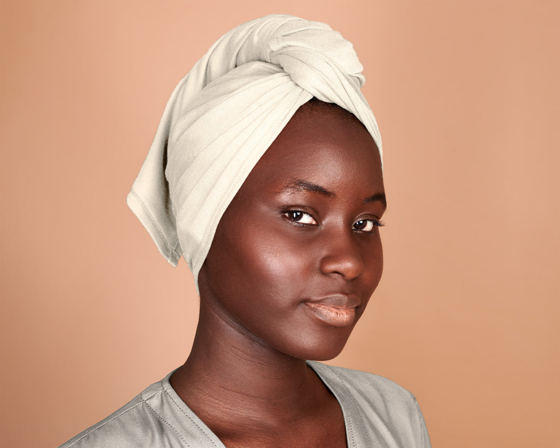 Woman wearing a T-Shirt Hair Towel for Curly, Wavy, and Straight Hair - Soft, Absorbent, and Eco-Friendly, in a white cream color, wrapped around her head, against a beige background
