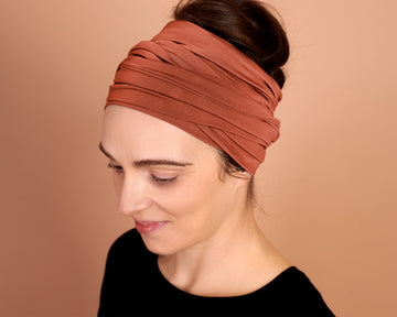 Woman wearing a rust-colored head wrap, against a beige background