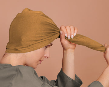 A person wearing a yellow t-shirt hair towel hood, tying it around their head.