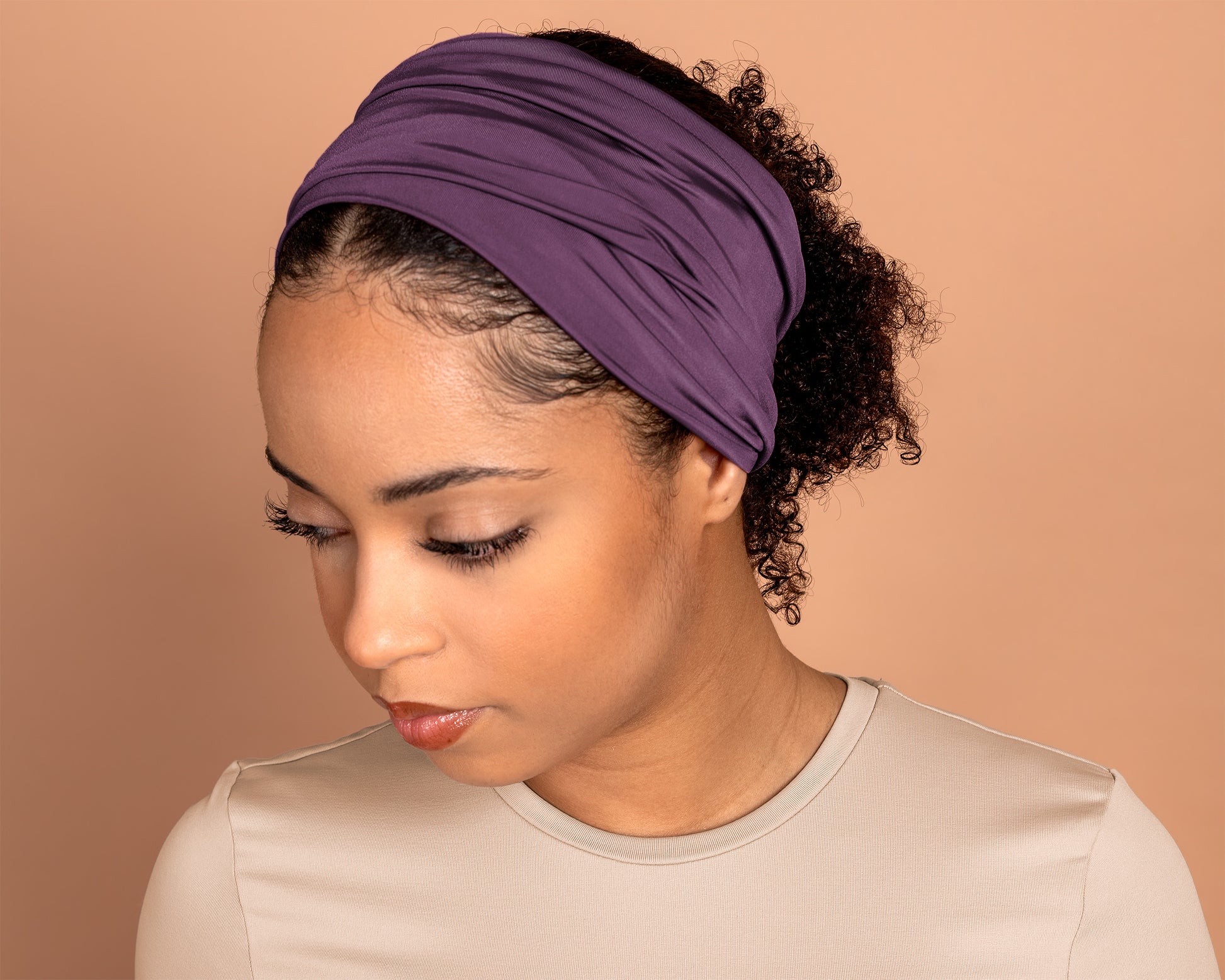A woman wearing a wide, gathered Boho Headband  in Light Plum with her hair pulled back, shown from the chest up against a solid warm beige background.