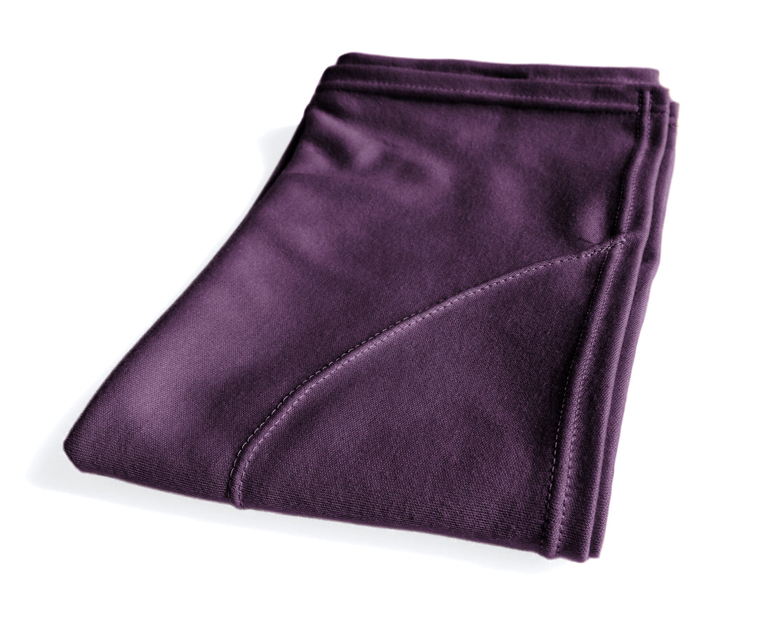 A person with curly hair using a purple  plum t-shirt hair towel to dry their hair in the bathroom.