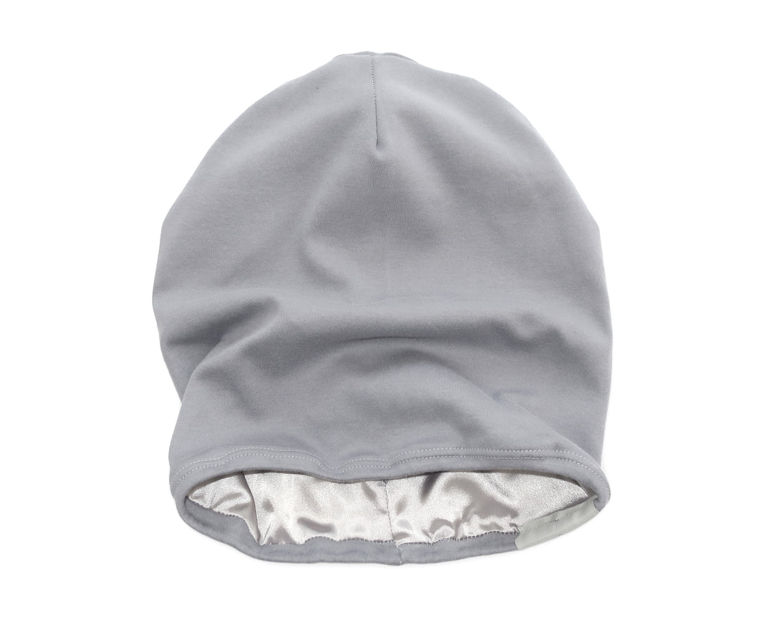 Woman wearing a gray satin-lined beaniewith a blurred outdoor background