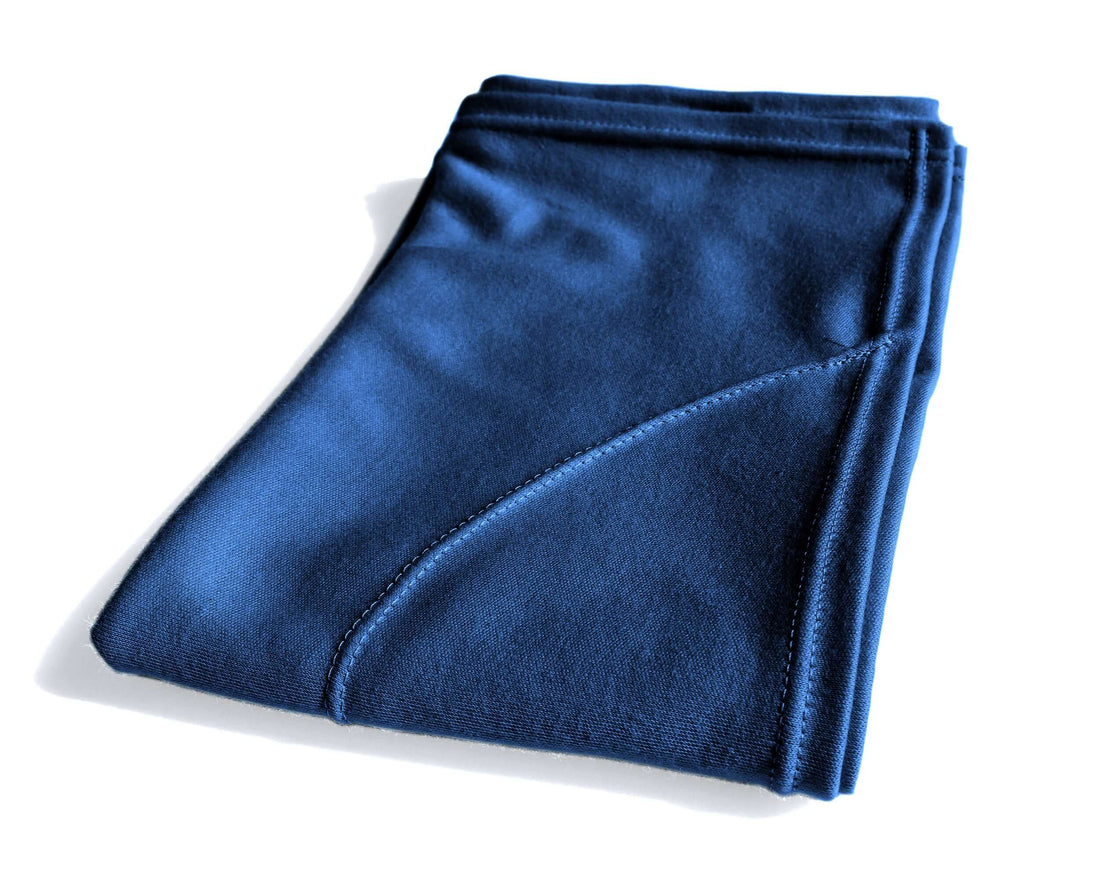 A woman with curly hair using a blue t-shirt hair towel on one side of their head, standing in a bathroom setting.