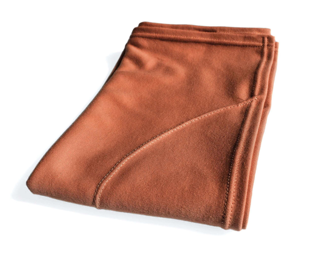 A person with curly hair is using an orange t-shirt hair towel to dry their hair in the bathroom.