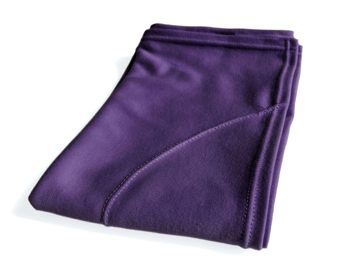 A person with curly hair using a purple t-shirt hair towel to dry their hair in the bathroom.