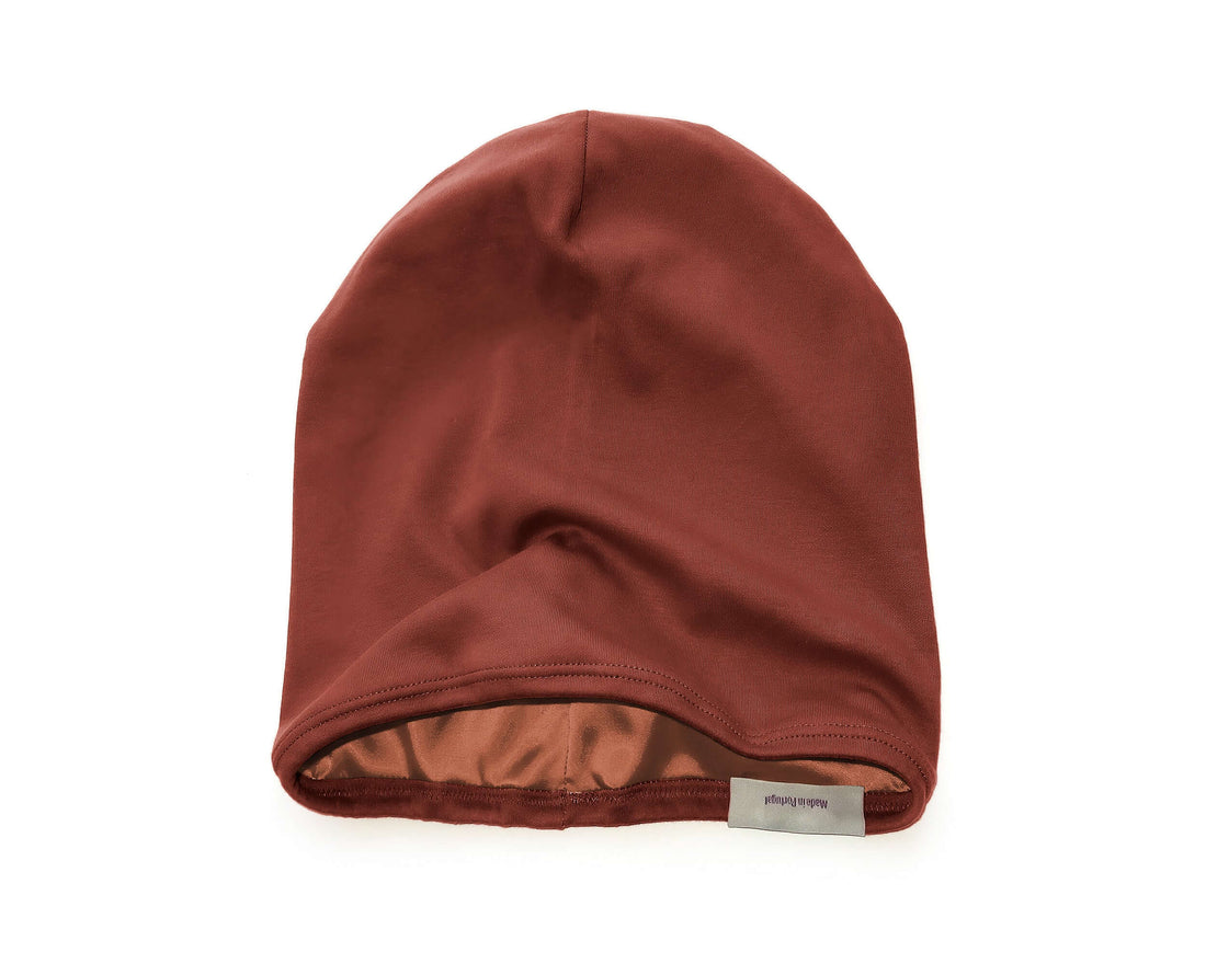 woman wearing a Satin-Lined Beanie for Women and Men - Soft and Warm Beanie with Satin Lining to Protect Hair in Burnt Orange.  She is shown in profile against a blurred outdoor background of green hills and blue sky.
