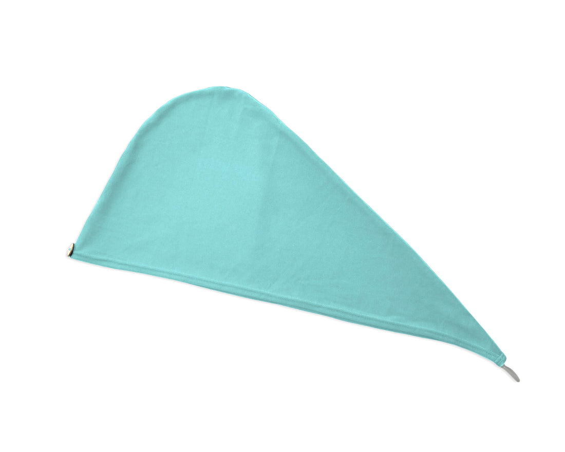 A woman wearing a T-shirt Eco-Friendly Hair Towel Hood, for Curly, Wavy, and Straight Hair - Soft, Absorbent in Aqua Blue, adjusting it with both hands. The cap has a small brown button closure on the back with a white drawstring.